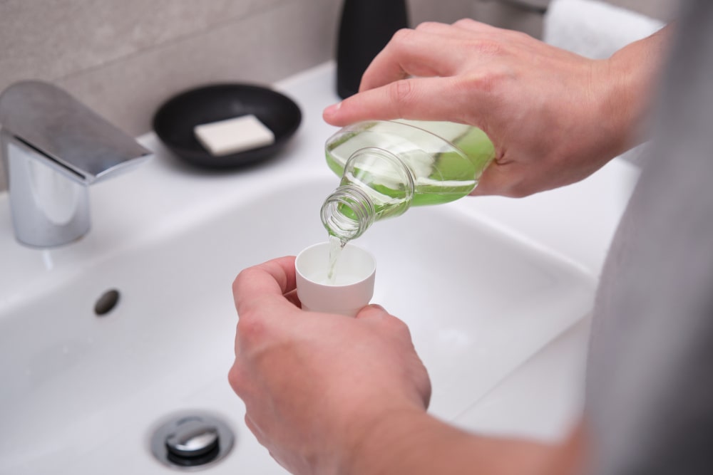 Man pouring green mouthwash into a bottle cap