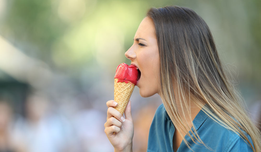 Woman feeling tooth pain when biting into cold food like ice cream